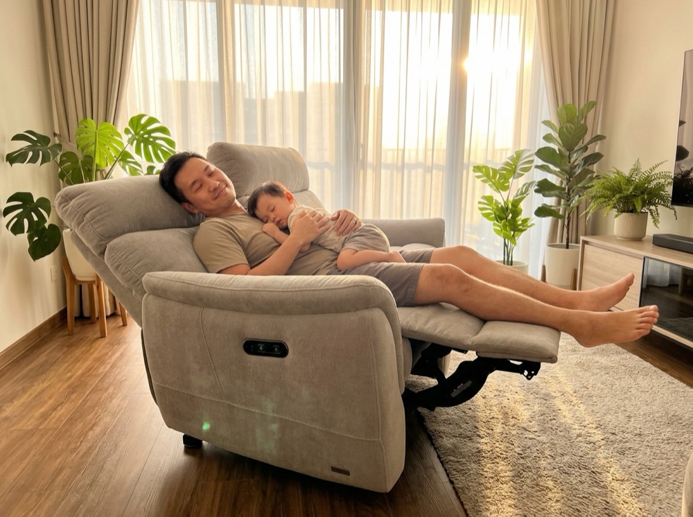 A dad reclined on the grey fabric recliner with toddler asleep on his chest